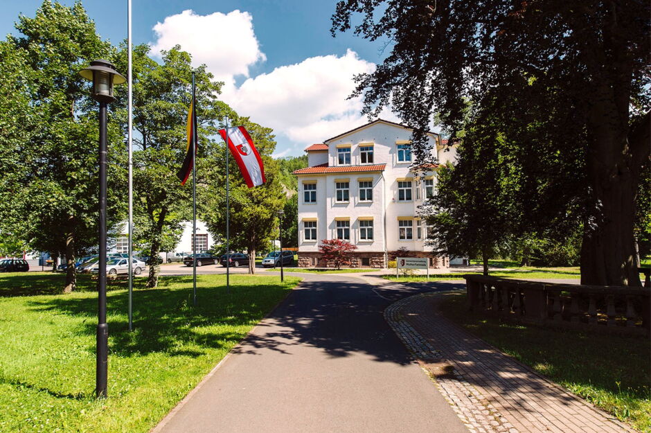 Gemeindeverwaltung Wutha-Farnroda - Rathaus, Frontalansicht im Sommer mit wehenden Fahnen